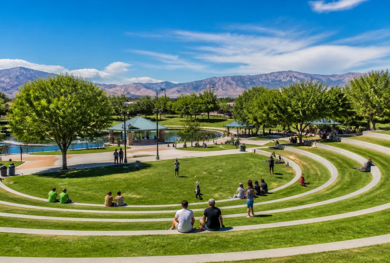 The grass amphitheater, shade trees, and pond at Craig Ranch Regional Park with mountains behind