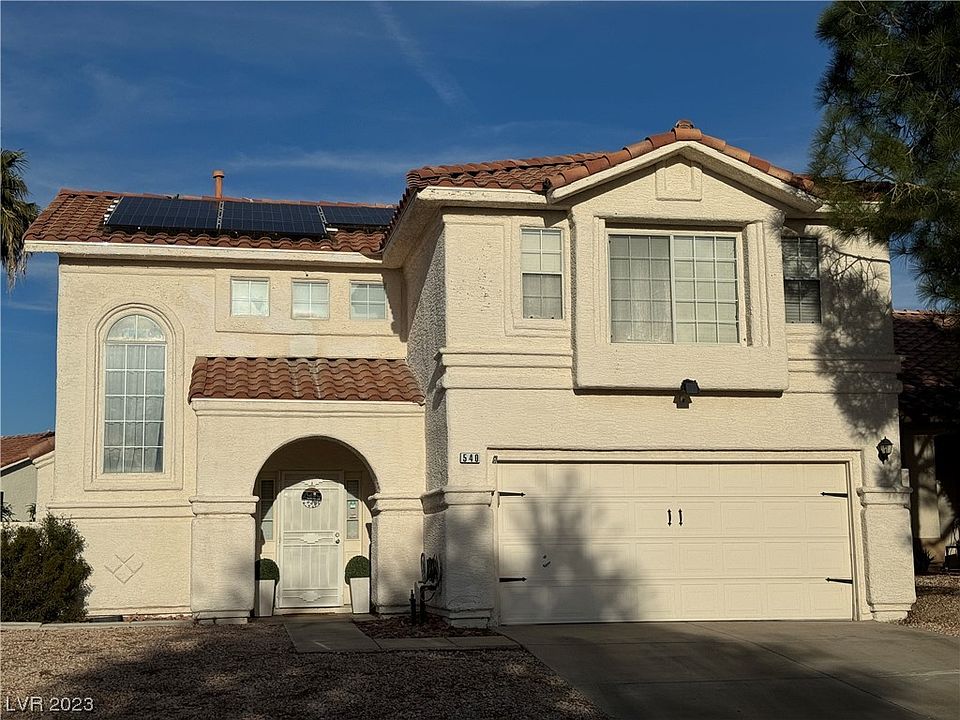 Two-story cream stucco home with a tile roof, rooftop solar panels, and an arched entry at 540 Landra Ln in Henderson